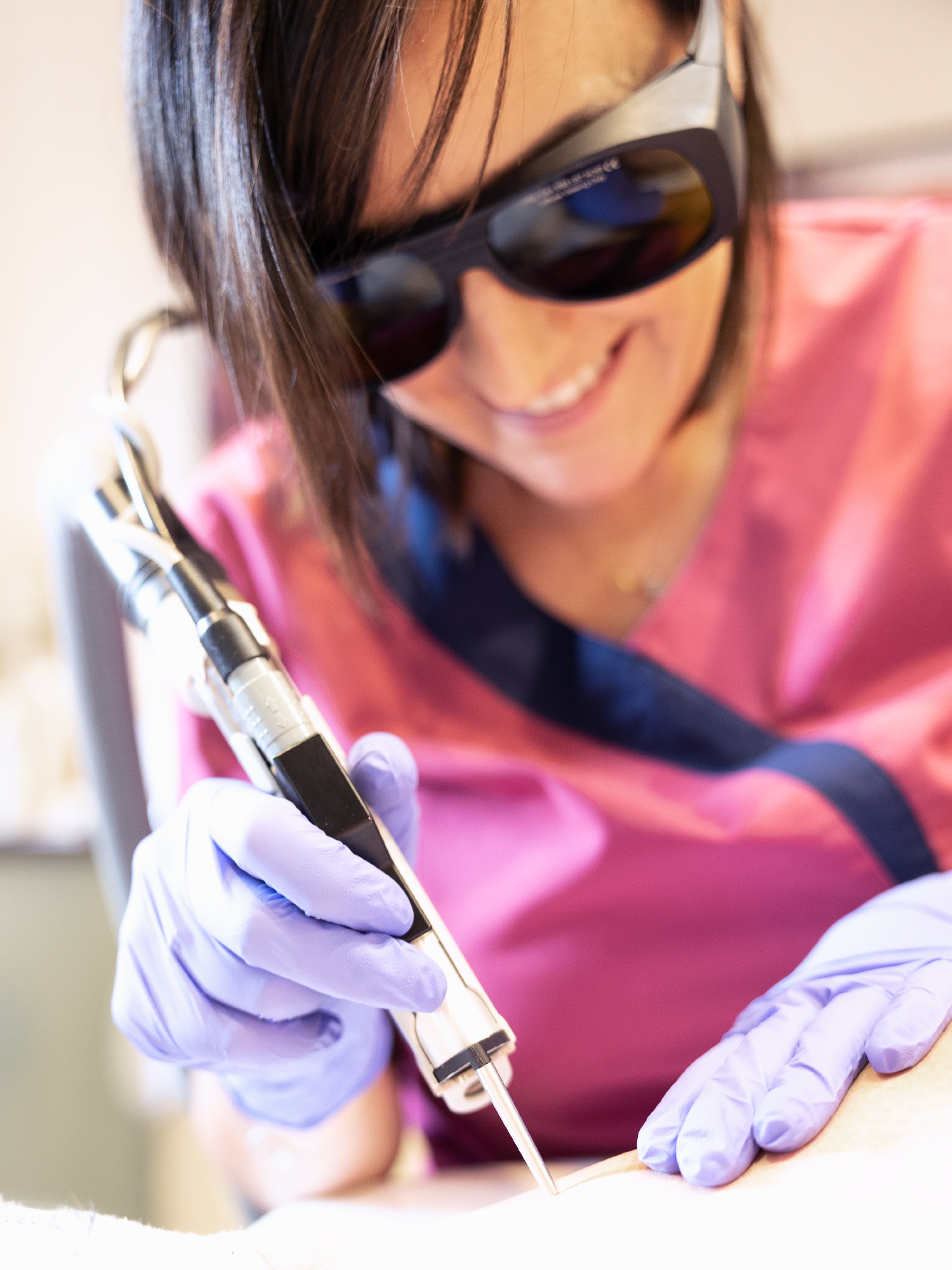 Laser-epilation-laseriste technicienne de laser avec lunette de protection blouse rouge réalisant une épilation laser sur une jambe